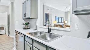 Een moderne keuken met een roestvrijstalen spoelbak, witte kastjes en een kleine potplant.
