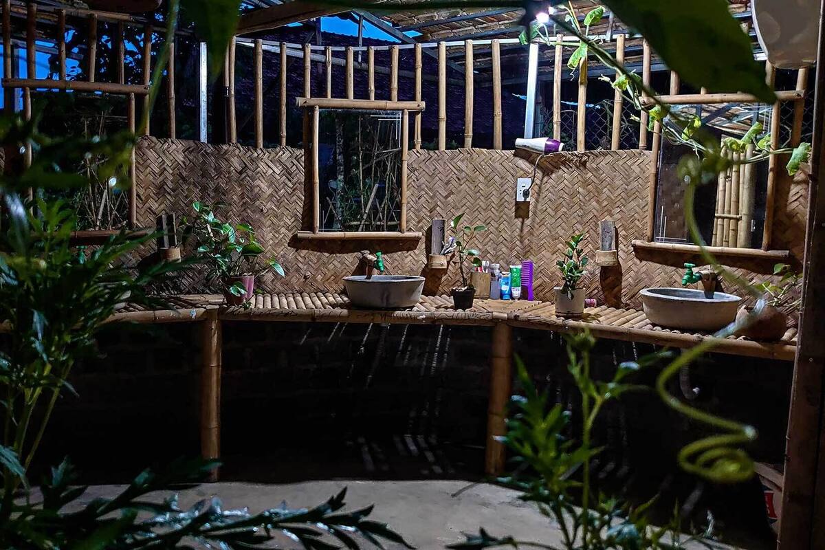 A rustic outdoor area with bamboo structures, potted plants, and a water feature.
