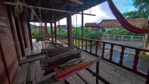 A wooden porch with a woven mat and a view of a river and houses. - MUONG PHANG HOMESTAY (Muong Phang)