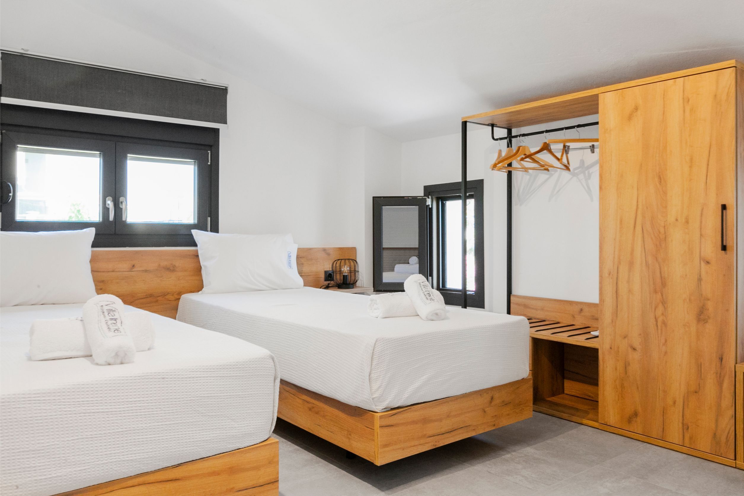 Quarto de hotel moderno com duas camas, um guarda-roupa de madeira, um espelho e uma janela com persianas.