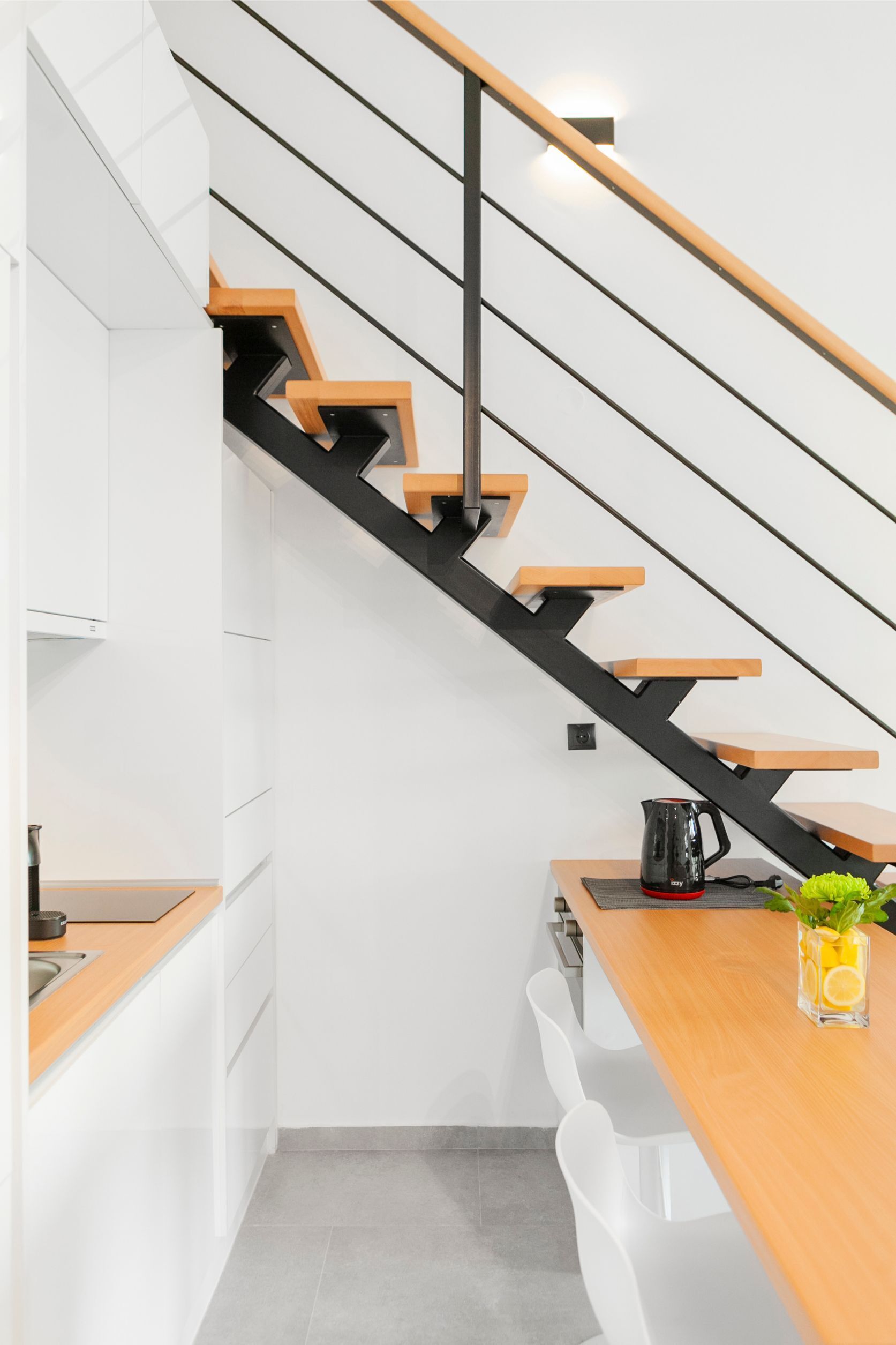 Una cocina moderna con armarios blancos, encimera de madera y una escalera negra con escalones de madera.