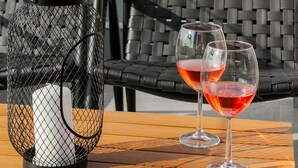 Una silla de mimbre y una mesa con un farol y dos copas de vino tinto, con vistas al mar.