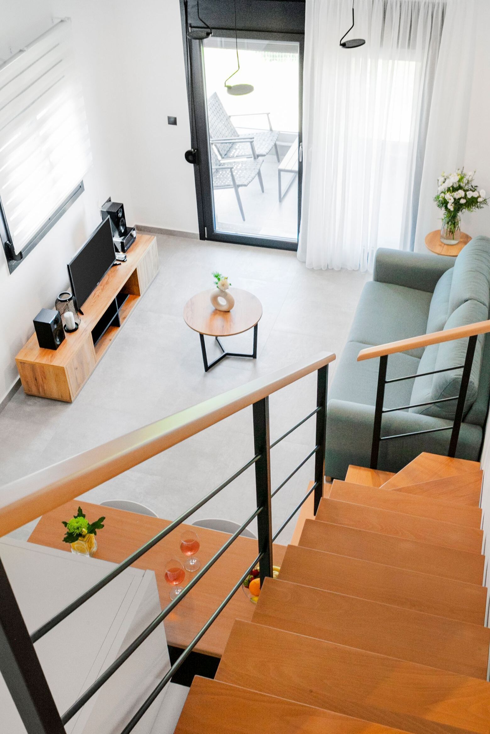 A modern living room with a sofa, a coffee table, and a TV on a wooden stand. There is a staircase leading to another level.