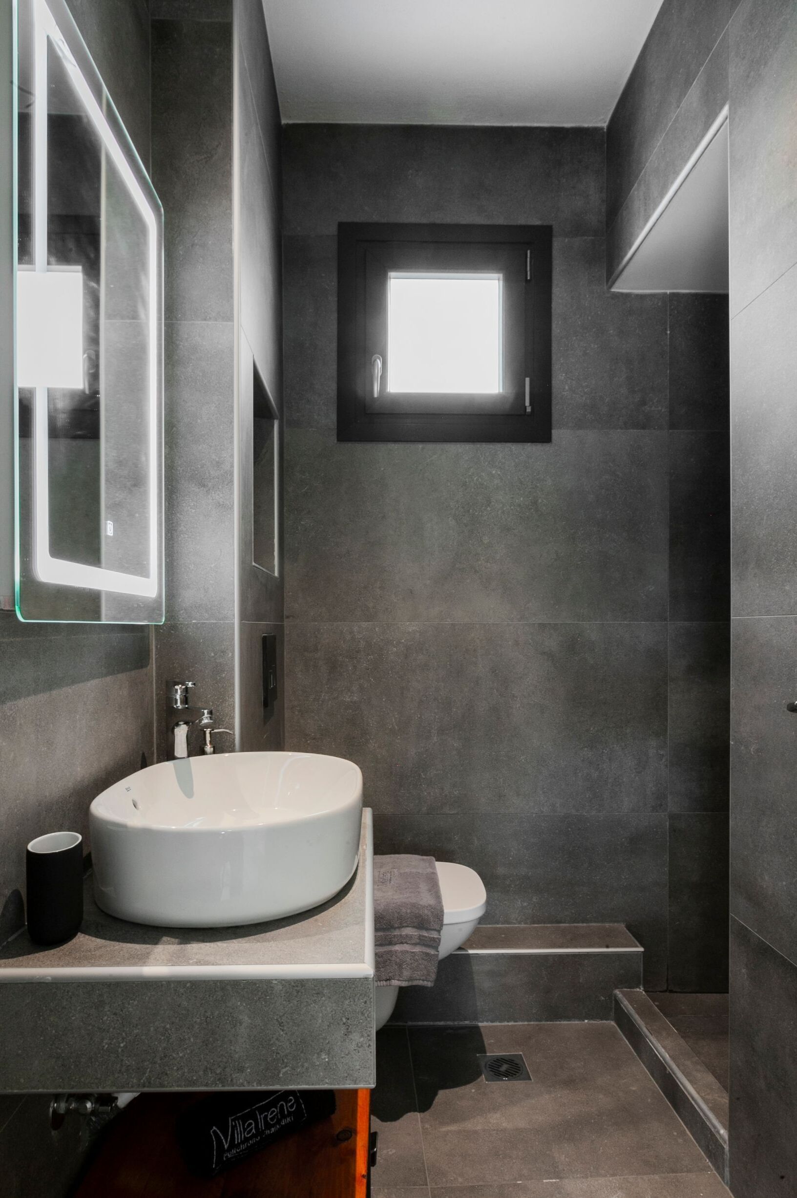 Une salle de bain moderne avec un grand lavabo blanc, un miroir et une fenêtre située au-dessus des toilettes.