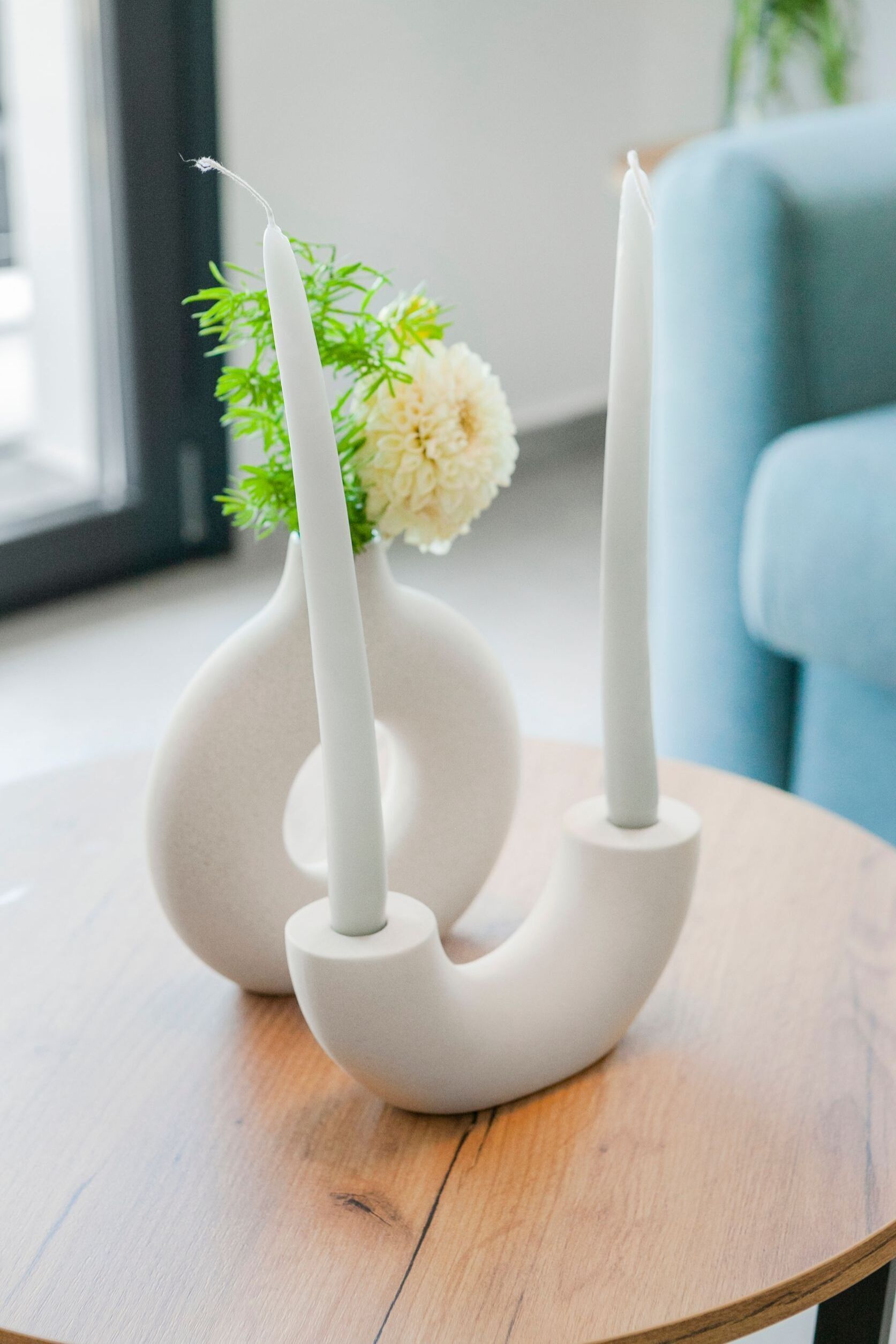 A white vase with two candles on a wooden table.