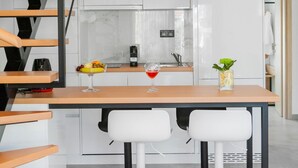 Una cocina moderna con armarios blancos, una escalera de madera y un comedor con dos taburetes blancos.