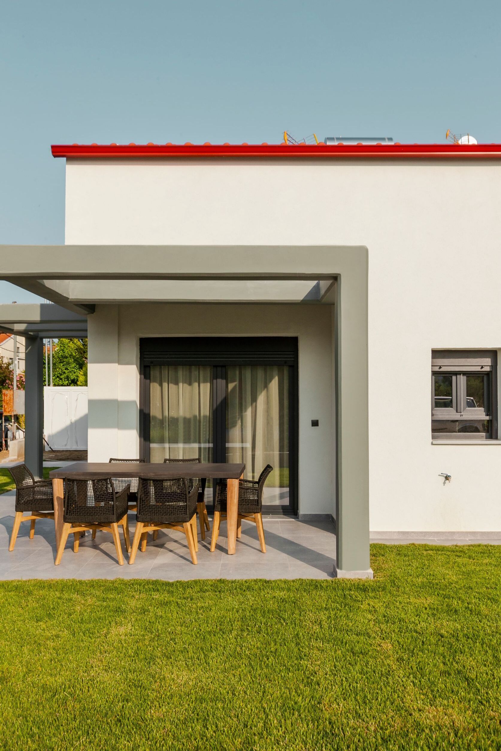 A modern house with a patio, a dining table with chairs, and a sliding glass door.