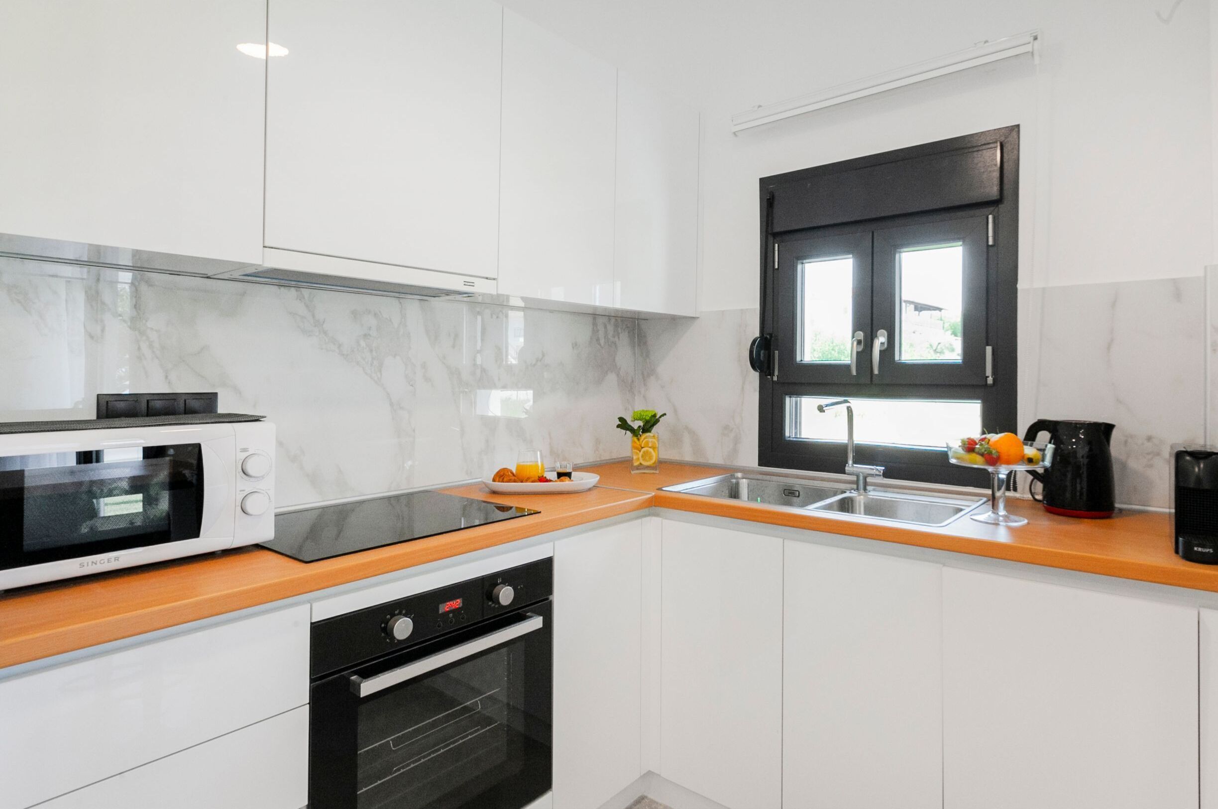 Una cucina moderna con mobili bianchi, un forno a microonde nero, un lavello e una finestra con cornice nera.