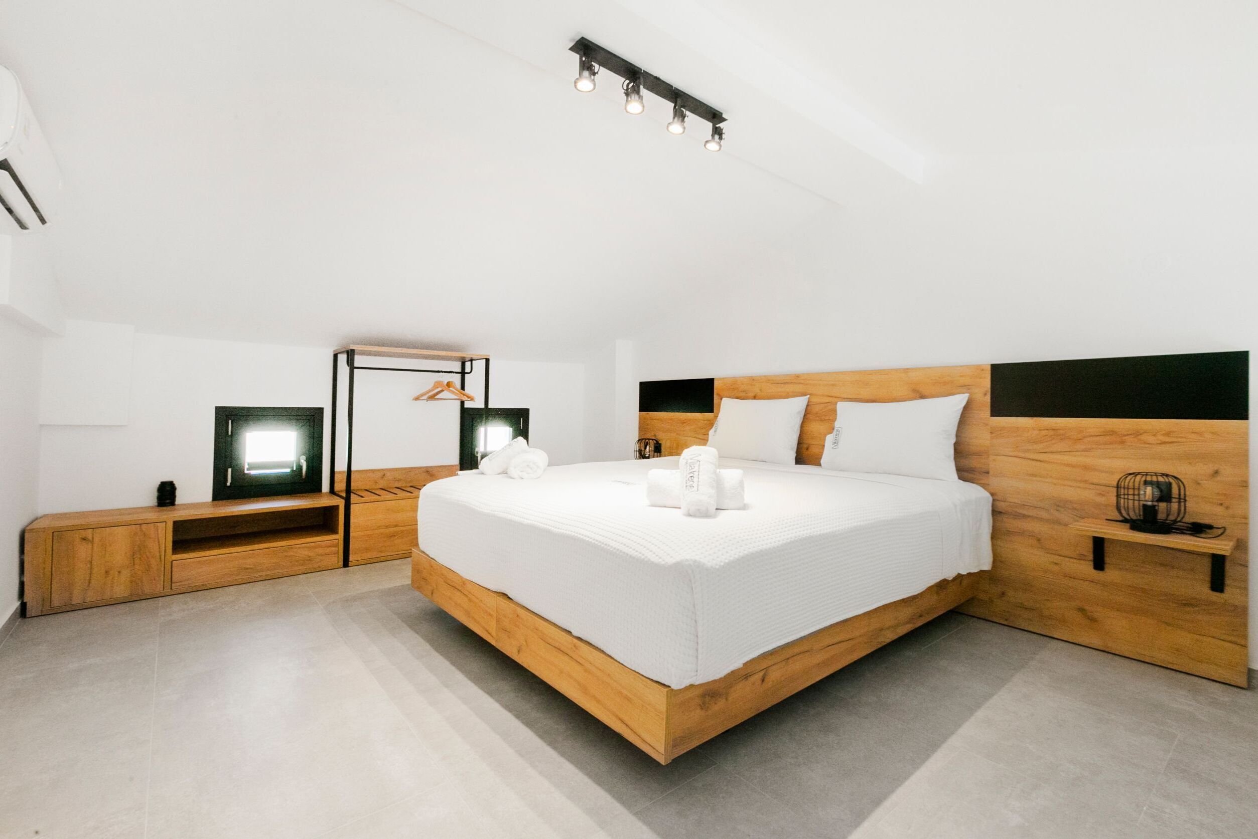 A modern bedroom with a wooden bed, bedside tables, a mirror, and a TV.