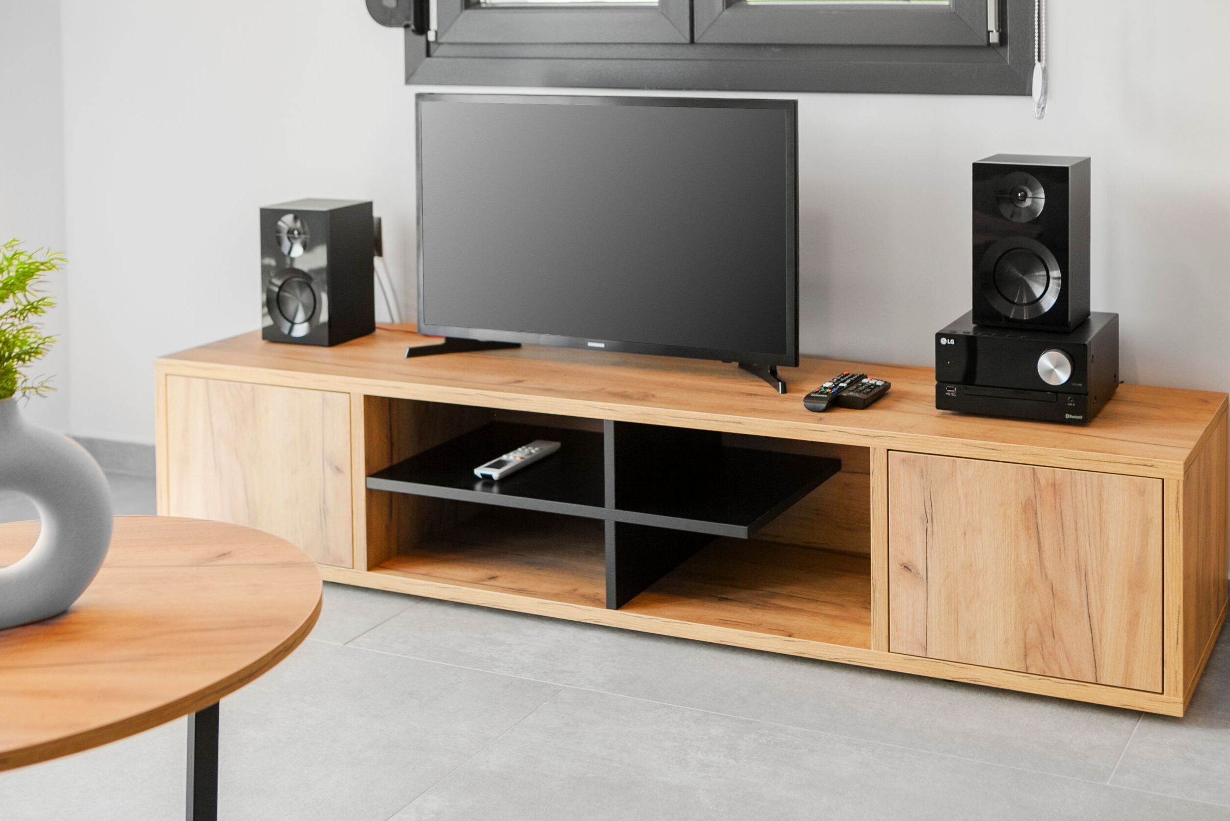 Un mueble moderno de entretenimiento con un televisor de pantalla plana, dos altavoces y un control remoto.