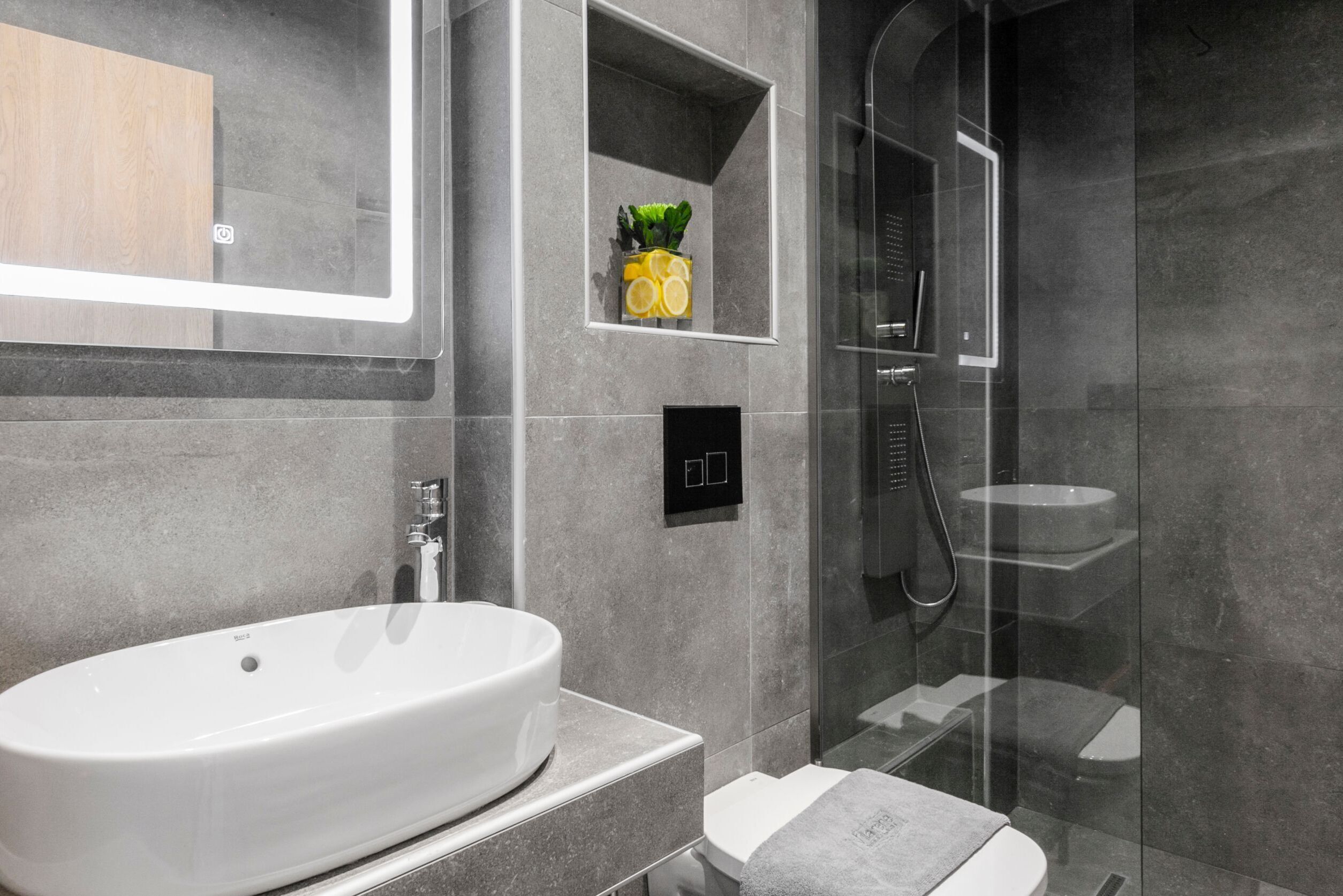 Een moderne badkamer met een vrijstaand bad, een douche met glazen wanden en een klein plankje met toiletartikelen.