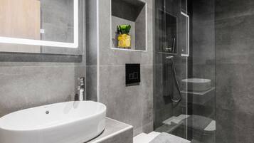 Een moderne badkamer met een vrijstaand bad, een douche met glazen wanden en een klein plankje met toiletartikelen.