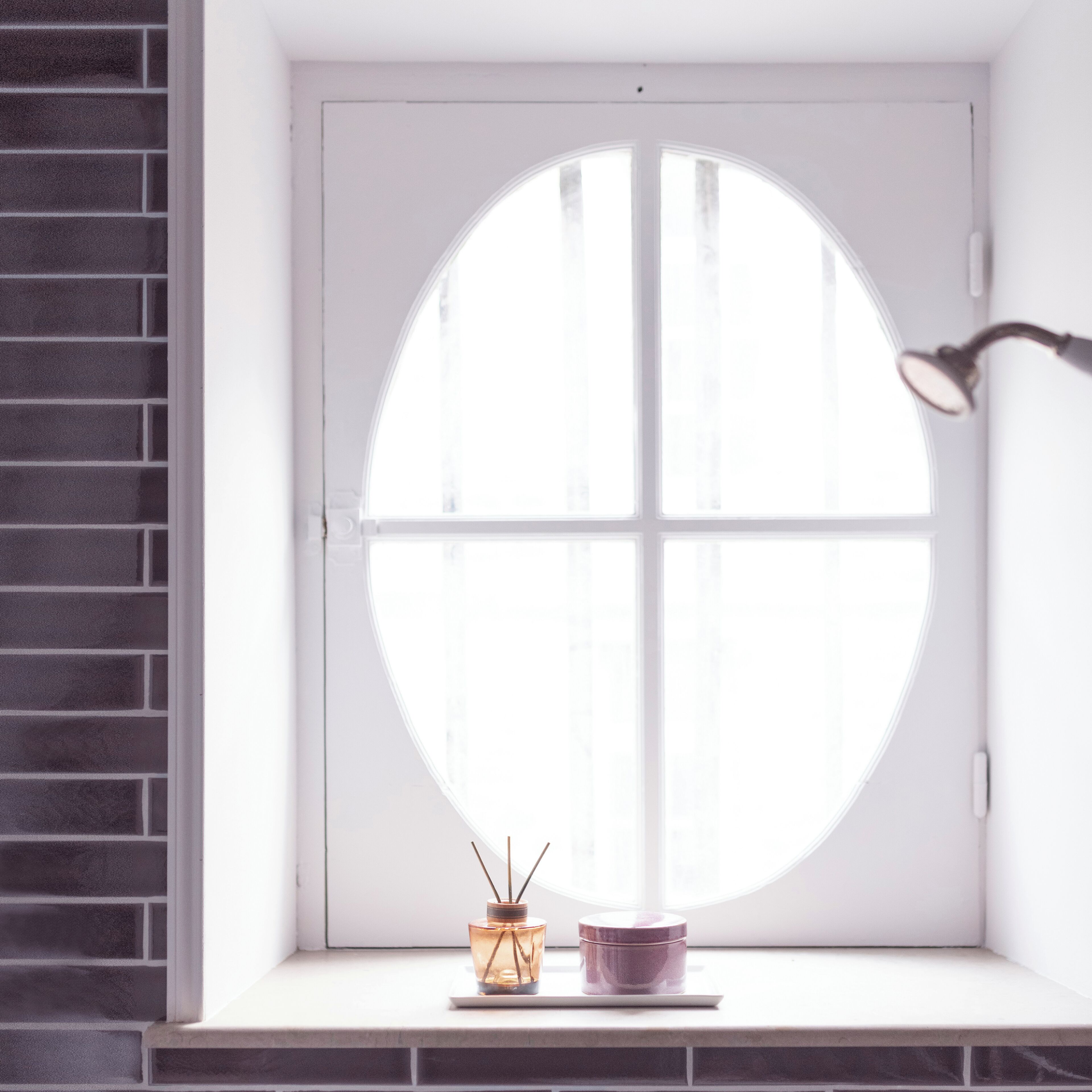 A window with a round view, a small table with a candle and a container, and a brick wall.