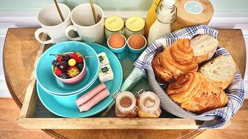 Una bandeja de desayuno con cruasanes, mermelada, queso y un bol de fruta.