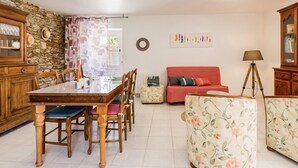 A dining area with a wooden table and chairs, a red sofa, and a floral armchair. - Renovated Cottage Near Marshes, 12 km from Beach, Private Terrace, Garden, WiFi, Baby-Friendly (Villeneuve-en-Retz)