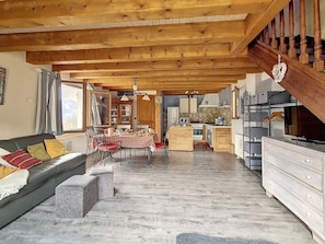 A cozy living room with a sofa, a dining table, and a kitchen area with wooden cabinets and a staircase.
