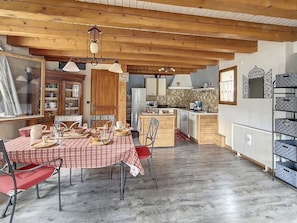 A cozy kitchen with wooden beams, a dining table set with red and white checkered tablecloth, and a view into the adjacent dining area.