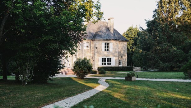 A stone building with a sloped roof, surrounded by a well-maintained lawn and trees. - Belle Propriété au Calme, à la Campagne Avec Parc et Étangs (Le Mesnil-Véneron)