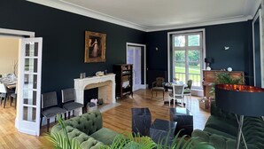 A spacious living room with a fireplace, green sofas, and a large window offering a view of the outdoors. - Belle Propriété au Calme, à la Campagne Avec Parc et Étangs (Le Mesnil-Véneron)
