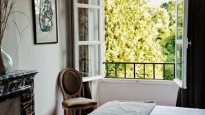A bedroom with a bed, a chair, a fireplace, and a window with a view of trees. - Belle Propriété au Calme, à la Campagne Avec Parc et Étangs (Le Mesnil-Véneron)
