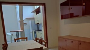 A dining area with a table and chairs, a kitchen in the background, and a wooden cabinet with drawers. - Cecchi Mansion (Nardò)