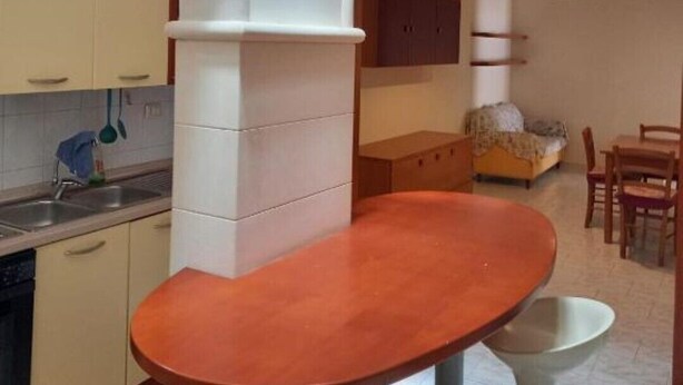A compact kitchen with a built-in oven, a dining area with a round table and chairs, and a visible ceiling light fixture. - Cecchi Mansion (Nardò)