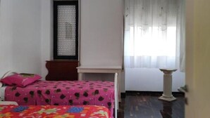 A room with two beds, a window with sheer curtains, a small table, and a ceiling light fixture. - Cecchi Mansion (Nardò)