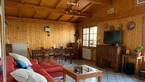 Ein Holzinterieur mit einem roten Sofa, einem Glastisch, einem Essbereich und einem Fernseher.