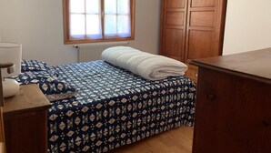 Ein Schlafzimmer mit einem Bett, einem Fenster mit Vorhängen, einem Heizkörper und einem Holzschrank.