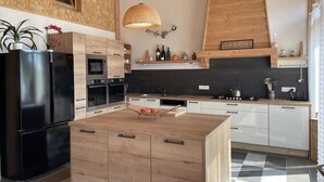 A modern kitchen with wooden cabinetry, a black refrigerator, and a central island with a woven light fixture above. - Rustic cottage with shared pool and pets allowed, sleeps 15 (Blomard)