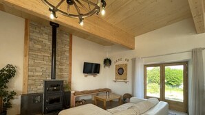 A cozy living room with a stone fireplace, a sofa, a TV, and a dartboard. - Rustic cottage with shared pool and pets allowed, sleeps 15 (Blomard)