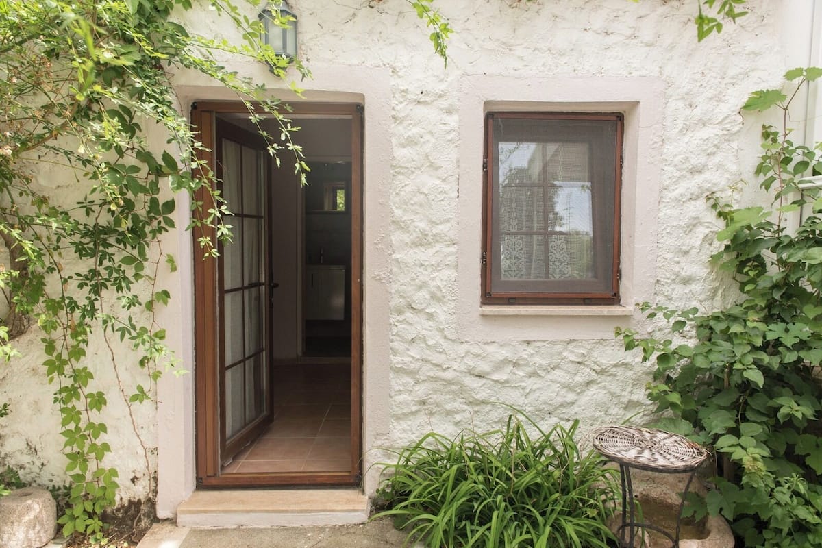 A rustic building with a wooden door and a window, surrounded by greenery.