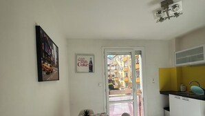 A dining area with a table and chairs, a kitchen with a yellow wall, and a door leading outside. - T1 bis Proche Centre-ville, Campagne et Commodités (Rodez)