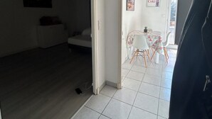 An open-plan living area with a dining table and chairs, a sofa, and a small kitchen area. - T1 bis Proche Centre-ville, Campagne et Commodités (Rodez)