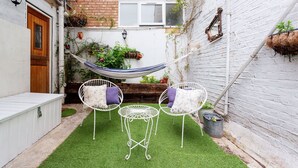 A small backyard with artificial grass, white metal chairs, a small table, and a hammock. - Harmonious Hideaway, by Veeve (London)