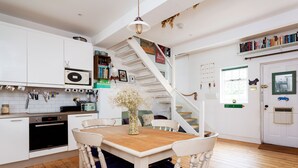 A kitchen with white cabinets, a wooden dining table with blue cushions, and a white staircase. - Harmonious Hideaway, by Veeve (London)