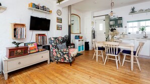 A living room with a wooden floor, a TV, a floral armchair, a bookshelf, and a dining area with a table and chairs. - Harmonious Hideaway, by Veeve (London)