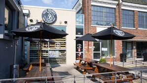 An outdoor seating area with wooden tables and black umbrellas, a brick building with a sign reading "Jack Brown's Brewery," and a clear sky.