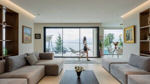 A modern living room with a large sliding glass door leading to an outdoor seating area with a view of the sea. - The Luxury Villa by PikHost (Shkodër)