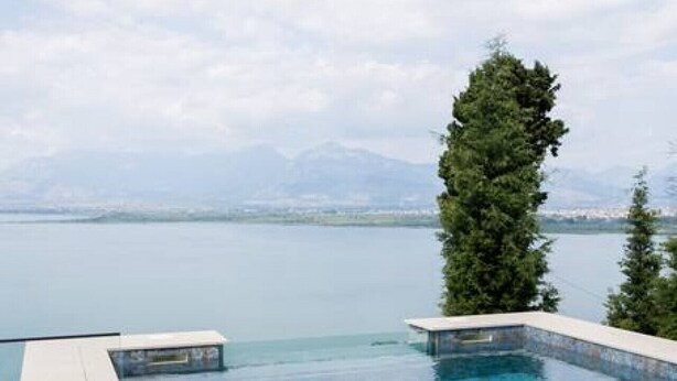 A clear blue infinity pool with a view of a mountain range and a body of water. - The Luxury Villa by PikHost (Shkodër)