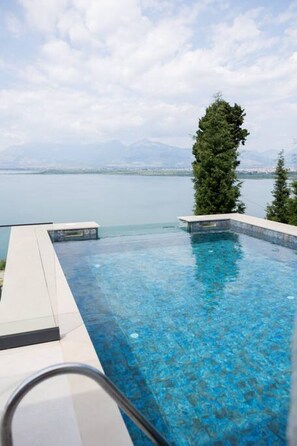 A clear blue infinity pool with a view of a mountain range and a body of water. - The Luxury Villa by PikHost (Shkodër)