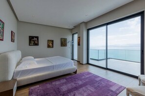 A modern bedroom with a large bed, a purple rug, and a balcony with a view of the sea. - The Luxury Villa by PikHost (Shkodër)