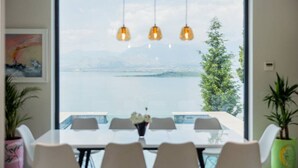 A dining area with a large window overlooking a body of water and mountains. There are four chairs around a table with a vase of flowers. - The Luxury Villa by PikHost (Shkodër)