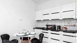 Une cuisine moderne avec des meubles blancs, un plan de travail noir et un coin repas comprenant deux chaises noires et une table ronde.