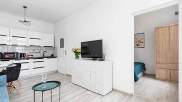 Eine moderne Küche mit weißen Schränken, einem schwarzen Fernseher auf einem weißen Schrank, einem Essbereich mit einer blauen Couch und einem kleinen runden Tisch mit einem Glas.