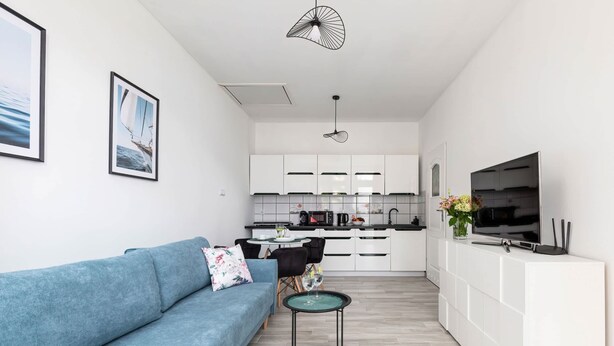 Un salon moderne avec un canapé bleu, une petite table ronde et un téléviseur posé sur un meuble blanc.