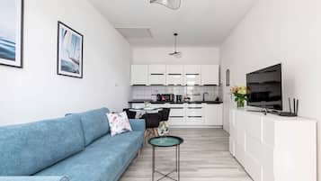Ein modernes Wohnzimmer mit einem blauen Sofa, einem kleinen runden Tisch und einem Fernseher auf einem weißen Schrank.