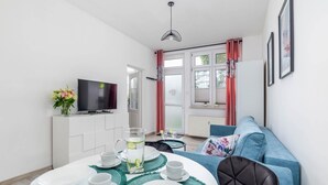 Un salon moderne avec un téléviseur, une table à manger dressée avec des assiettes et des tasses, un canapé et une fenêtre avec des rideaux.