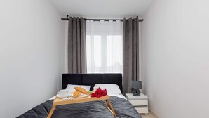 Una cama bien hecha con una bandeja de alimentos para el desayuno, una mesita de noche con una lámpara y una ventana con cortinas.