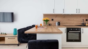 Una cocina moderna con armarios blancos, encimera de madera, horno negro y una zona de comedor con sillas negras.